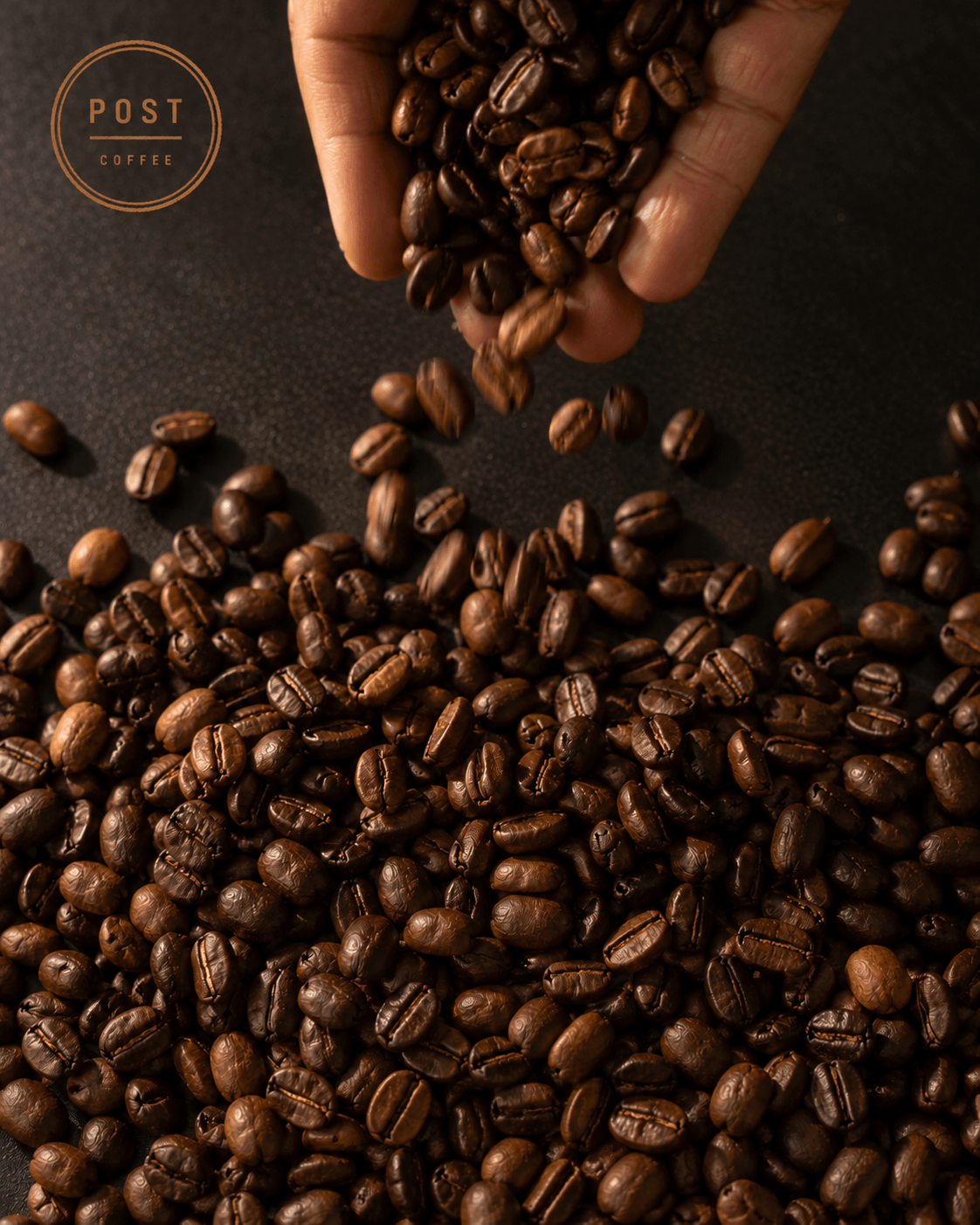 Roasted coffee beans falling from a hand onto a dark surface.