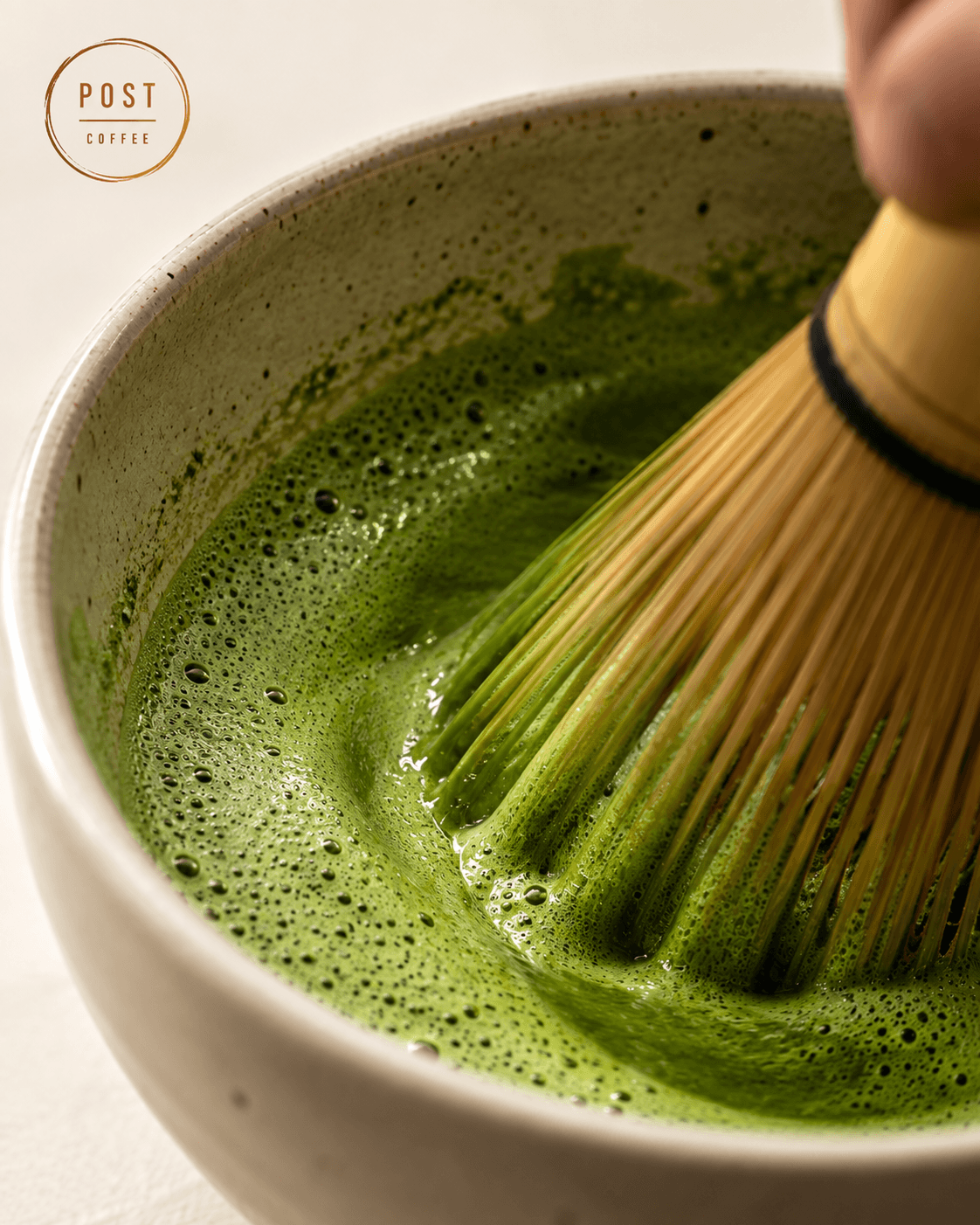 Matcha being whisked in a ceramic bowl with a bamboo whisk.