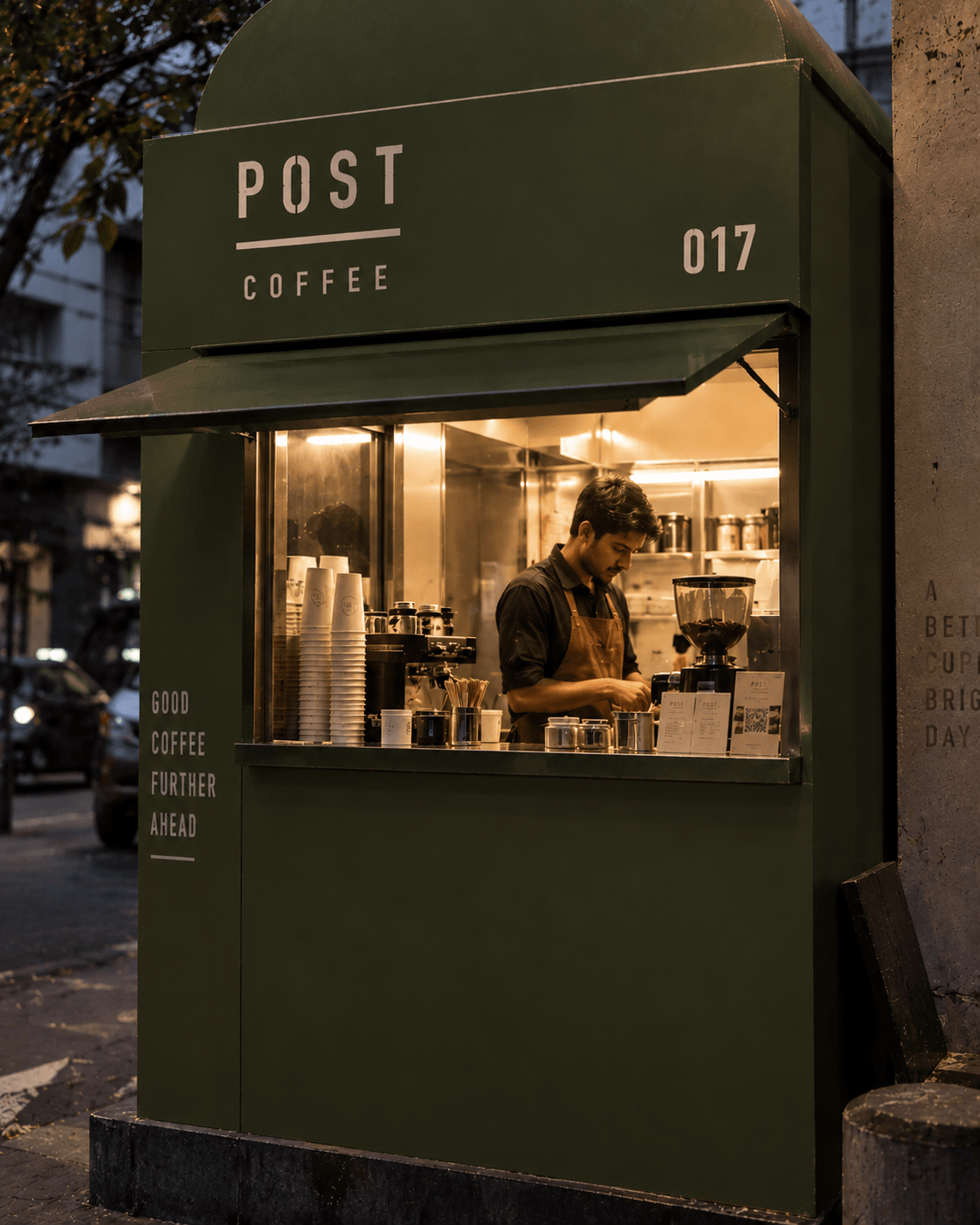 An olive green Post Coffee kiosk lit from within at dusk.